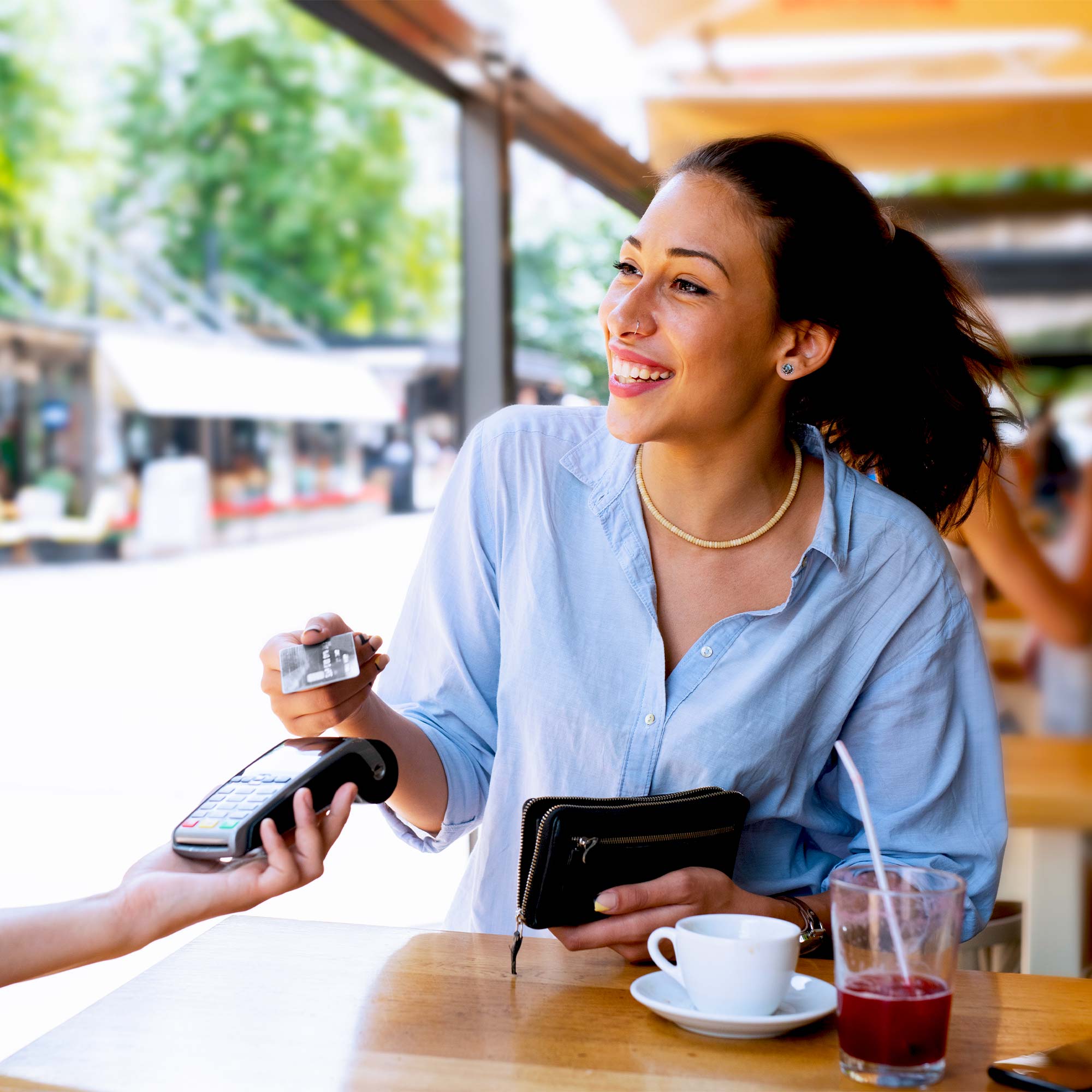 A woman wearing a blue shirt smiles as she pays with her debit card.